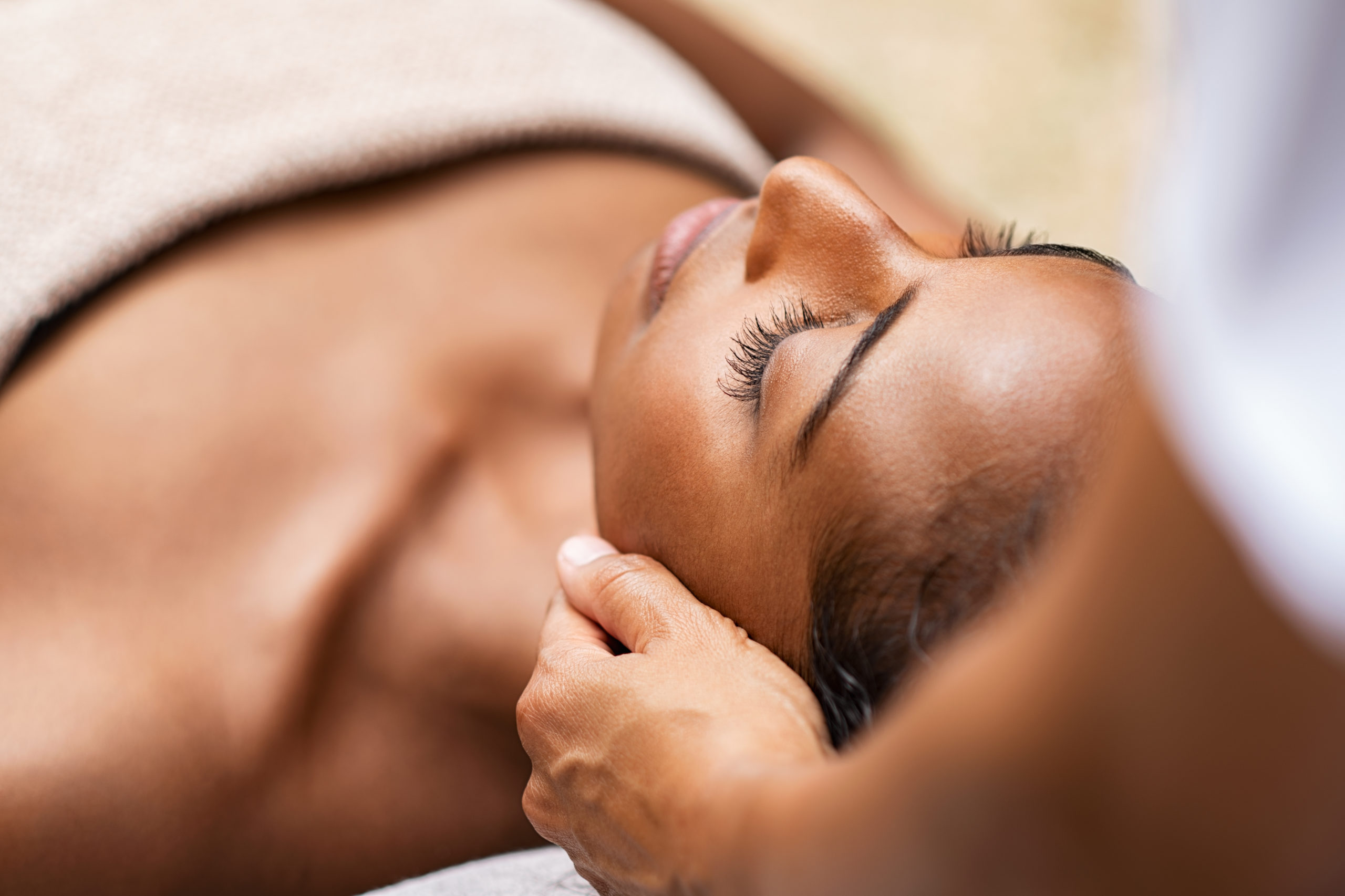 Beautiful african woman getting face massage in beauty spa. Black girl with closed eyes relaxing in outdoor spa while getting head massage. Serene woman relaxing outdoor in a beauty center.