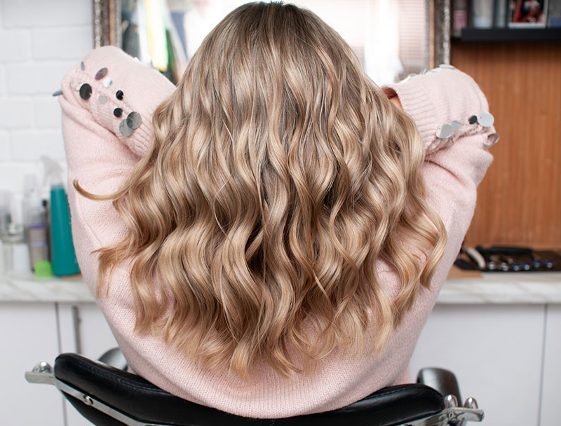 Blonde woman with chic curls view from the back in a beauty salon