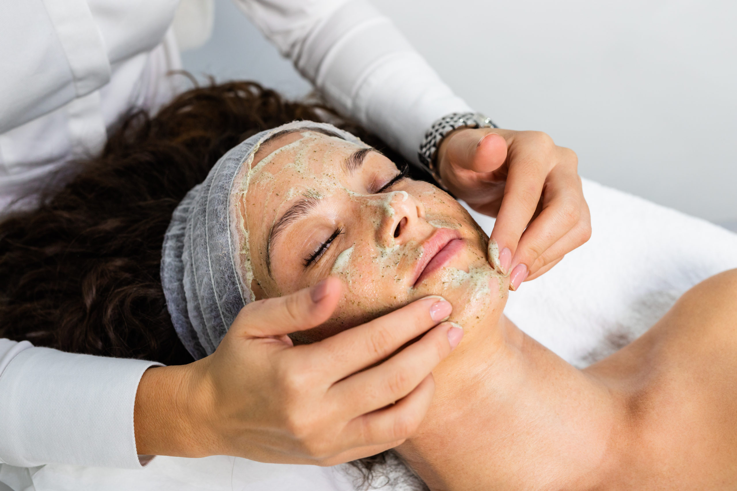 Beautiful woman receiving natural green peel facial mask with re